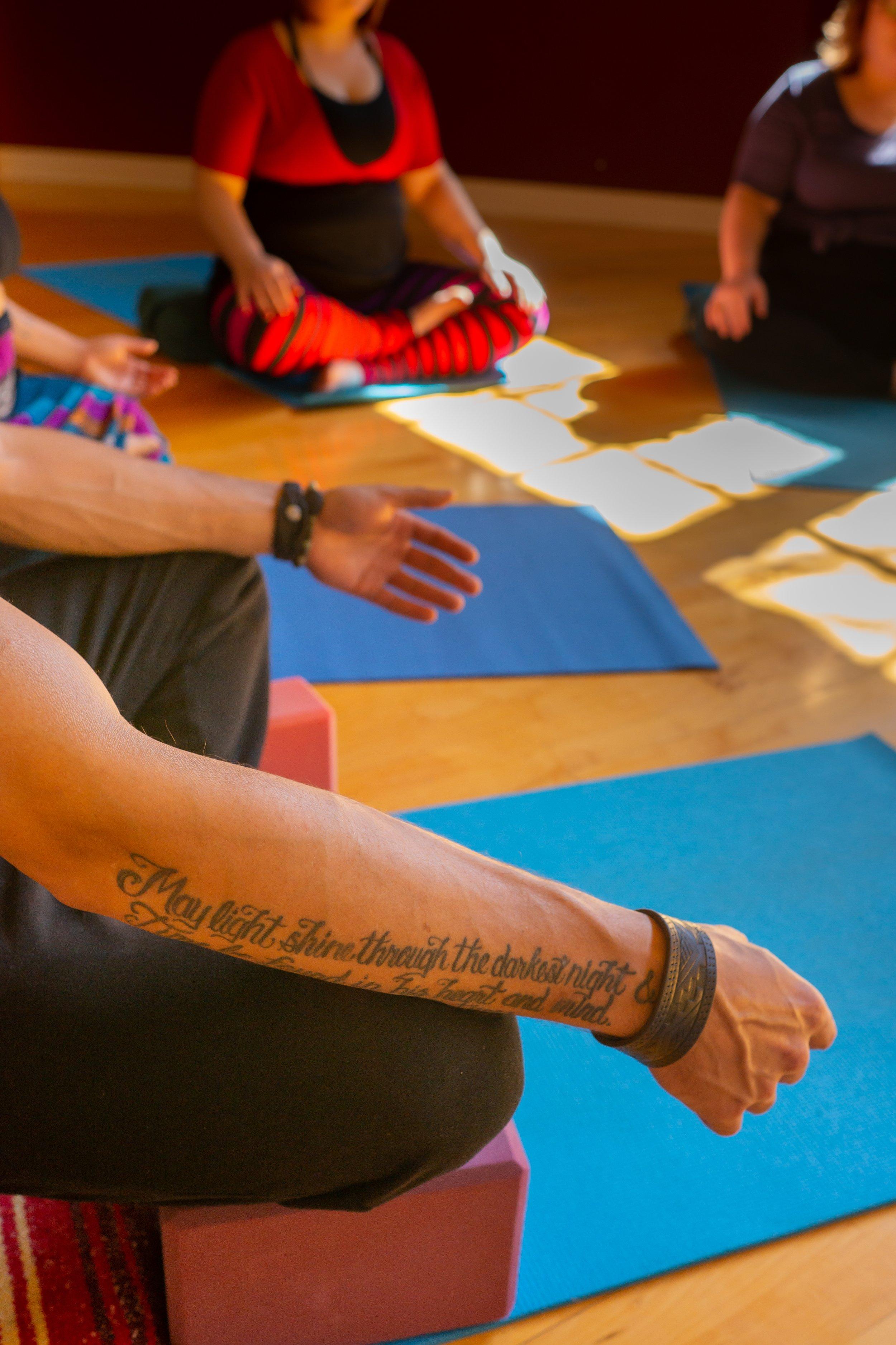 Group of large bodied people in  bright colorful activewear sitting crosslegged on yoga mats with relaxed arms